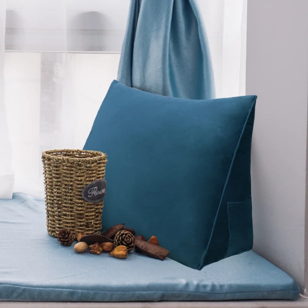 Granatowa poduszka klinowa umieszczona w przytulnym, zaaranżowanym miejscu do siedzenia przy oknie, idealnym do czytania.