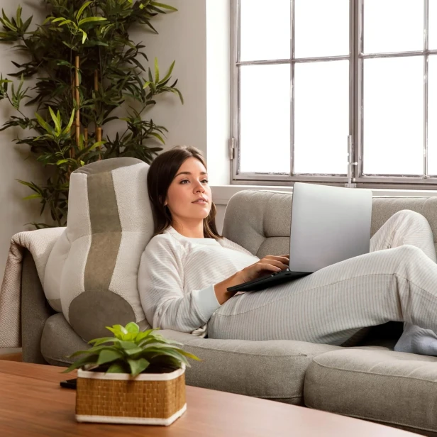 Młoda kobieta leży wygodnie na sofie oparta o Ergonomiczną Poduszkę pod Plecy z Falistym Kształtem.