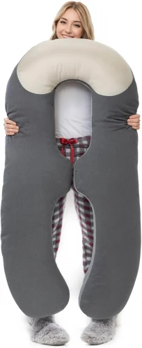 Młoda kobieta trzymająca dużą, profilowaną poduszkę ciążową w kształcie litery U. Szara