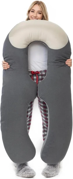 Młoda kobieta trzymająca dużą, profilowaną poduszkę ciążową w kształcie litery U. Szara