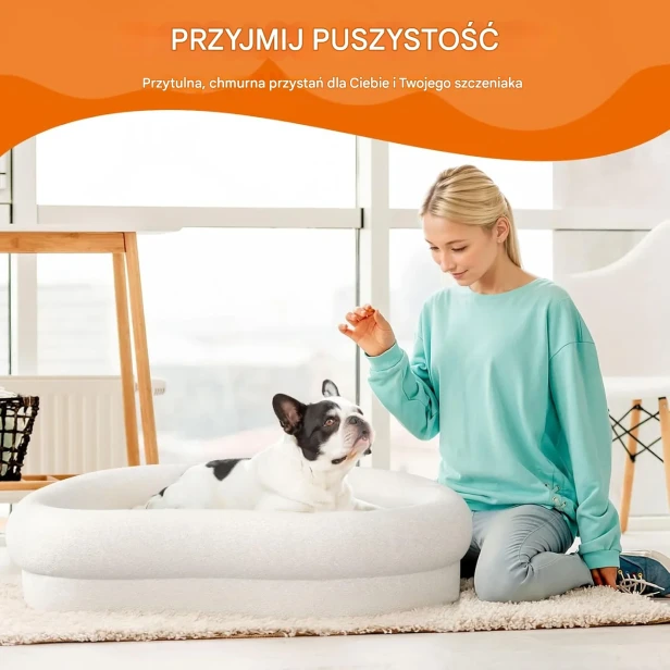 Kobieta klęcząca obok Buldoga Francuskiego, który leży w białym, puszystym legowisku.