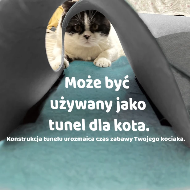Uroczy kot wchodzi do tunelu do zabawy, wykonanego z miękkiego, szarego materiału. Tunel, widoczny z perspektywy wejścia, służy do urozmaicenia kociej zabawy i aktywności.