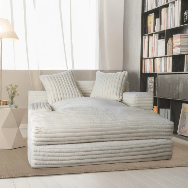 Szeroki, komfortowy szezlong w kremowym kolorze, pokryty miękką tkaniną sztruksową, ustawiony obok dużej biblioteczki, tworząc idealny kącik do czytania w jasnym, nowoczesnym wnętrzu.