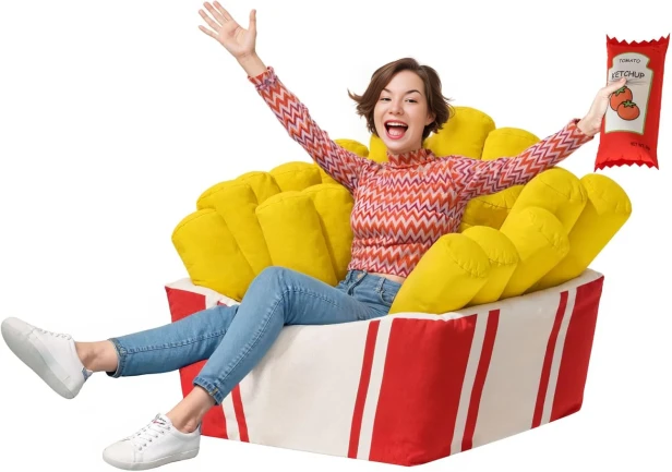 Duży, zabawny fotel worek sako w kształcie kartonu frytek z żółtymi frytkami, na którym siedzi uśmiechnięta kobieta, trzymająca pluszowy keczup.