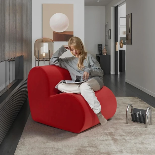 Młoda kobieta relaksuje się, czytając magazyn, siedząc na odważnym, czerwonym fotelu modułowym kształcie serca.