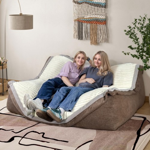 Dwie uśmiechnięte kobiety relaksują się na dużej, brązowo-beżowej  Modułowej Kanapie Wypoczynkowej z miękkim, prążkowanym materiałem.