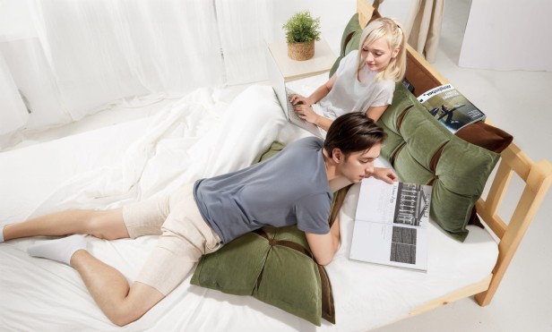 Para leżąca na łóżku korzystająca z Poduszek Zagłówkowych ze Schowkiem Zielono-Pomarańczowe