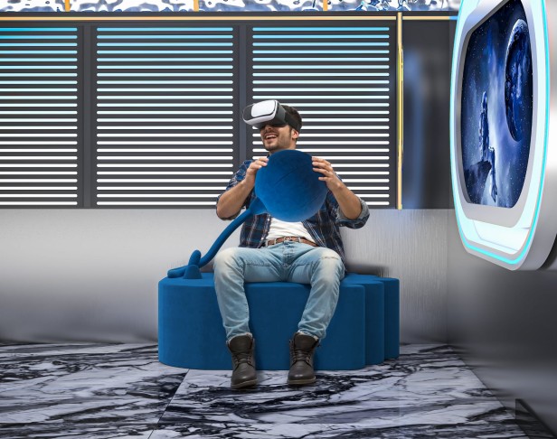 Mężczyzna siedzący i grający na Nowoczesnej Niebieskiej Pufie.