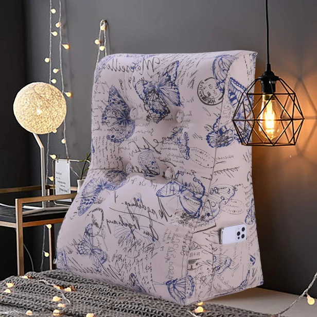 Wszechstronna Poduszka do Czytania Wzór Motyle Znajduje się na łóżku przykrytym szarym kocem i otoczona jest ciepłym, nastrojowym oświetleniem z lampek LED