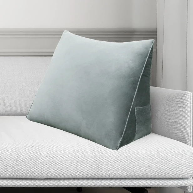 Szara poduszka wspierająca plecy, widoczna na tle kanapie w salonie.