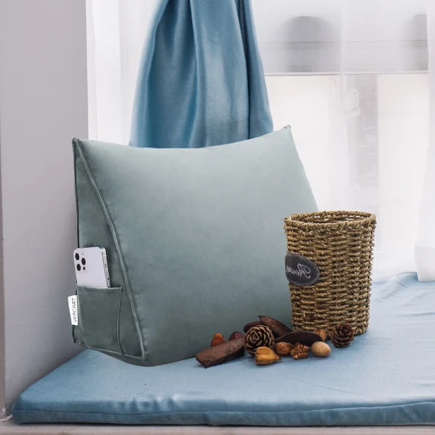 Szara poduszka klinowa umieszczona w przytulnym, zaaranżowanym miejscu do siedzenia przy oknie, idealnym do czytania.