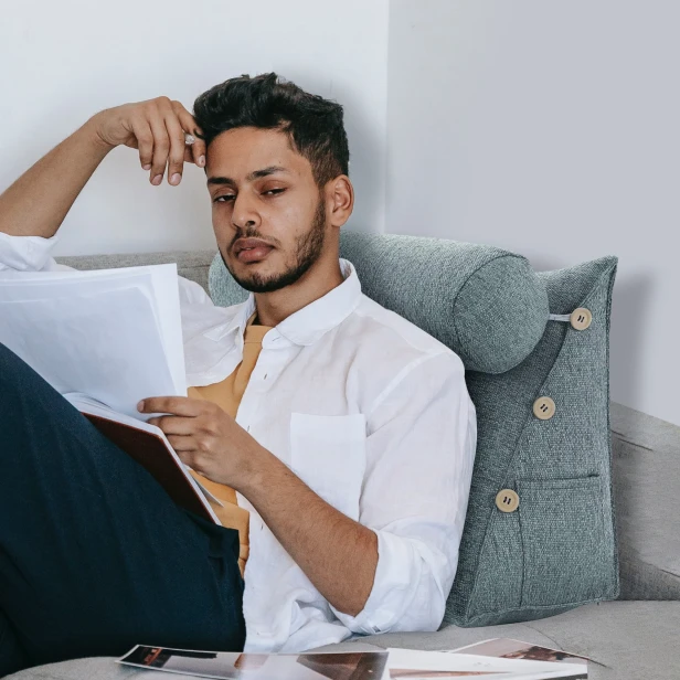 Mężczyzna opierający się o Modułowy Zagłówek z Wałkiem – Szary Len na łóżku.